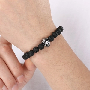 Macro detail of elastic lava stone beads and a vintage silver skull charm on a wrist