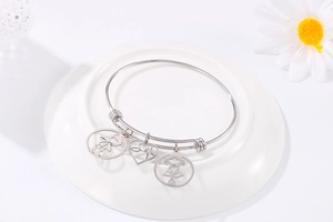 Close-up of stainless steel bangle with hollow boy, girl, and heart charms on a ceramic plate
