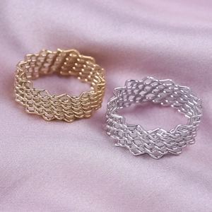Detail of woven mesh stainless steel rings in gold and silver on a soft silk background