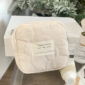 Detailed close-up of quilted cream makeup bag with soft texture and metallic zipper