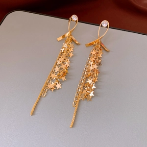Detail of golden tassel earrings featuring ribbon knots and star charms on long chains