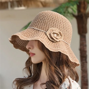 Women's light brown straw sun hat with flower pearl detail and wavy brim in outdoor sunlight