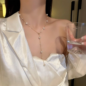 Detail of elegant Y-shaped gold necklace with white pearls worn on a female model