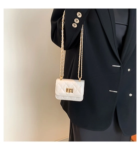 Detail of quilted white mini chain bag featuring a gold metal turn-lock and texture