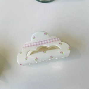 Detail of white cloud-shaped hair claw clip with pink floral patterns and plaid ribbon
