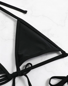 Detailed close-up of a black bikini top with adjustable straps on white marble