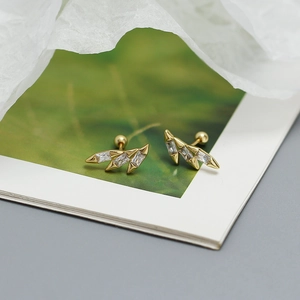 Macro shot of gold wing earrings with zircon stones on a leaf printed artistic background