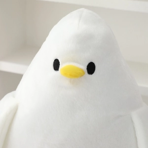 Close-up of the soft white plush pigeon toy featuring embroidered eyes and a yellow beak