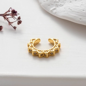 Macro shot of gold ear cuff with zircon inlay and gear shape on white pedestal