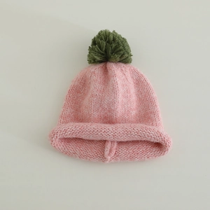 Detailed knit texture of light pink beanie with green faux fur pom-pom and rolled edge