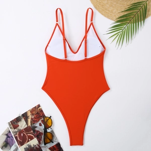 Flat lay of vibrant orange one-piece swimsuit with high-cut design and vacation accessories