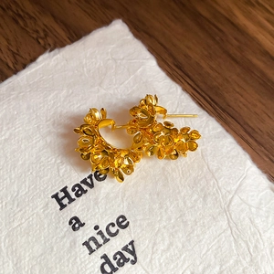 Detailed macro shot of golden C-shaped floral earrings on a textured card for women