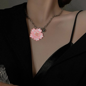 Primer plano de un collar plateado con colgante de flor rosa sobre un blazer negro