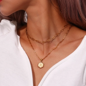 Detail showing a double-layered gold paperclip chain necklace with a hexagon R pendant