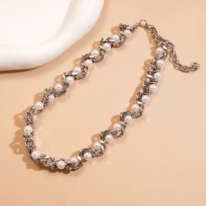 Detailed view of silver metal chain intertwined with white imitation pearls on beige backdrop