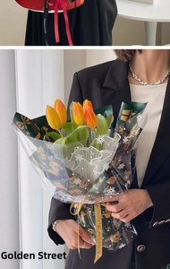 Close-up of orange tulips wrapped in green Christmas paper with golden snowflakes and lace