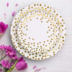 Close-up of white paper plates with gold foil dots on a light wood background