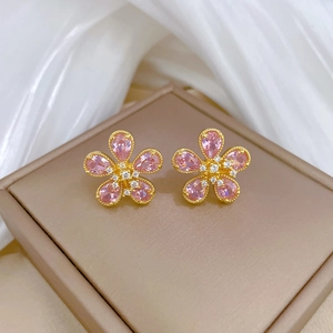 Gros plan de boucles d'oreilles fleurs en cristal rose et or sur fond de soie blanche