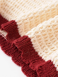 Macro view of cream and dark red knit fabric showing texture and scalloped edge detail