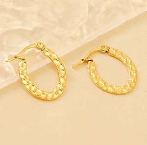 Close-up of gold-plated oval earrings with hammered texture and polished steel finish