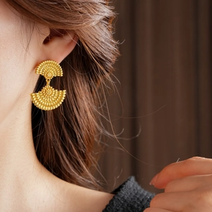 Gros plan de boucles d'oreilles éventail dorées avec texture portée par le modèle