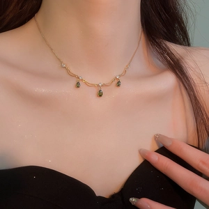 Dettaglio della collana placcata in oro con gemme verdi a goccia su una modella elegante
