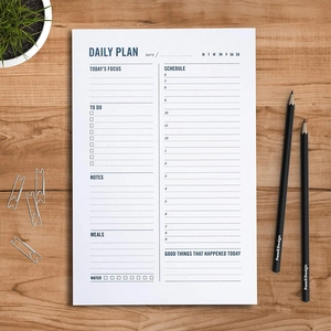 Detailed daily planner pad on wood desk featuring hourly schedule and habit tracker sections