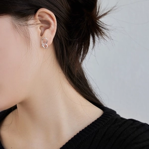 Detail of minimalist silver heart-shaped knot earring worn on the ear model