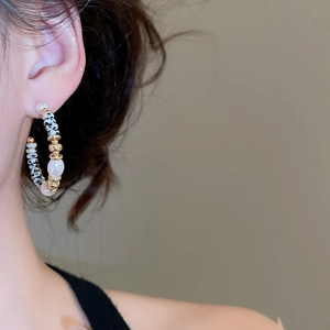 Dettaglio di orecchini a forma di C con perle e pietre indossati da una modella