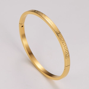 Macro view of gold Greek key pattern and hinge clasp on a stainless steel bangle