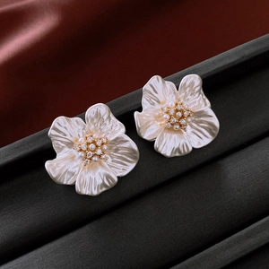 Close-up of pearl flower earrings with gold center and zircon detailing on a black stand