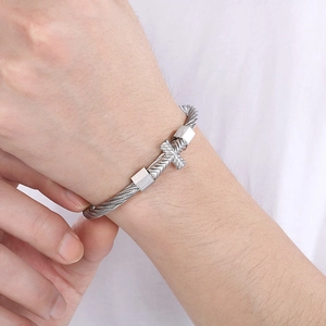 Close-up of silver twisted wire bangle featuring a cross charm on a model's wrist