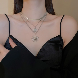 Detail of layered silver necklaces with sun face pendant and star charm on neck