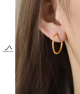 Close-up of model wearing gold stainless steel hoop earrings with elegant minimalist design