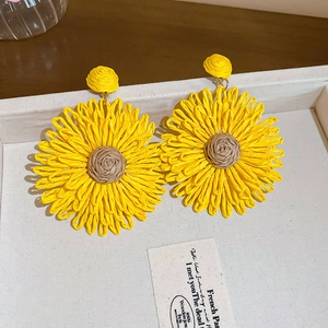 Close-up of large woven sunflower earrings with yellow petals on a beige jewelry tray
