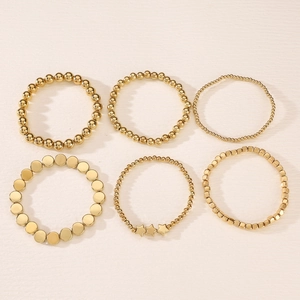 Dettaglio di sei braccialetti dorati con perline e maglie geometriche su base neutra