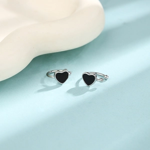 Detail of silver-bordered black heart ear cuffs on a light blue background