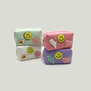 Detail of four preppy makeup bags featuring colorful chenille patches and gold metal zippers