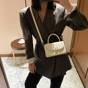 White minimalist mini crossbody bag with gold clasp shown on a model in a warm room