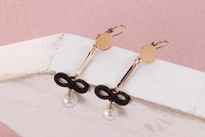Detail of rose gold dangle earrings with black infinity symbol and hanging white pearls