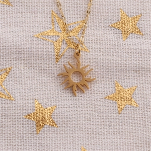 Vue détaillée du pendentif tournesol doré sur un tissu texturé avec motifs étoiles