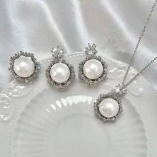 Close-up of elegant silver jewelry set with pearls and zircons on a white ceramic plate