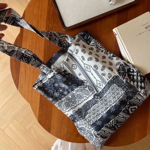 Sac fourre-tout en lin à motif cachemire noir et blanc posé à plat sur une table bois