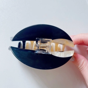 Black and marble white acetate hair claw clip with golden spring held by hand