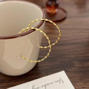 Polished golden twisted hoop earrings made of 925 silver on a cozy coffee cup edge