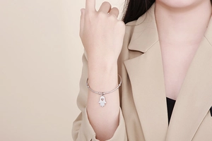Silver Hamsa palm charm bracelet with heart cutout worn on wrist with khaki blazer