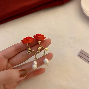 Close-up of red rose petal earrings with gold leaf stems and white baroque pearls