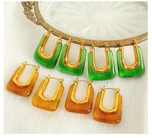 Detailed macro view of U-shaped resin earrings in emerald green and amber finishes