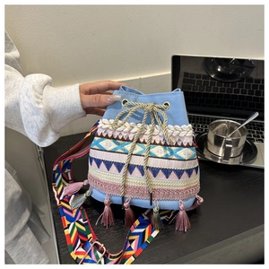Detail of light blue canvas bucket bag with colorful embroidery, tassels and ethnic strap