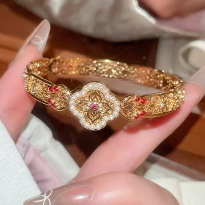 Detail of vintage gold bangle with red stone, white pearls, and filigree clover motif